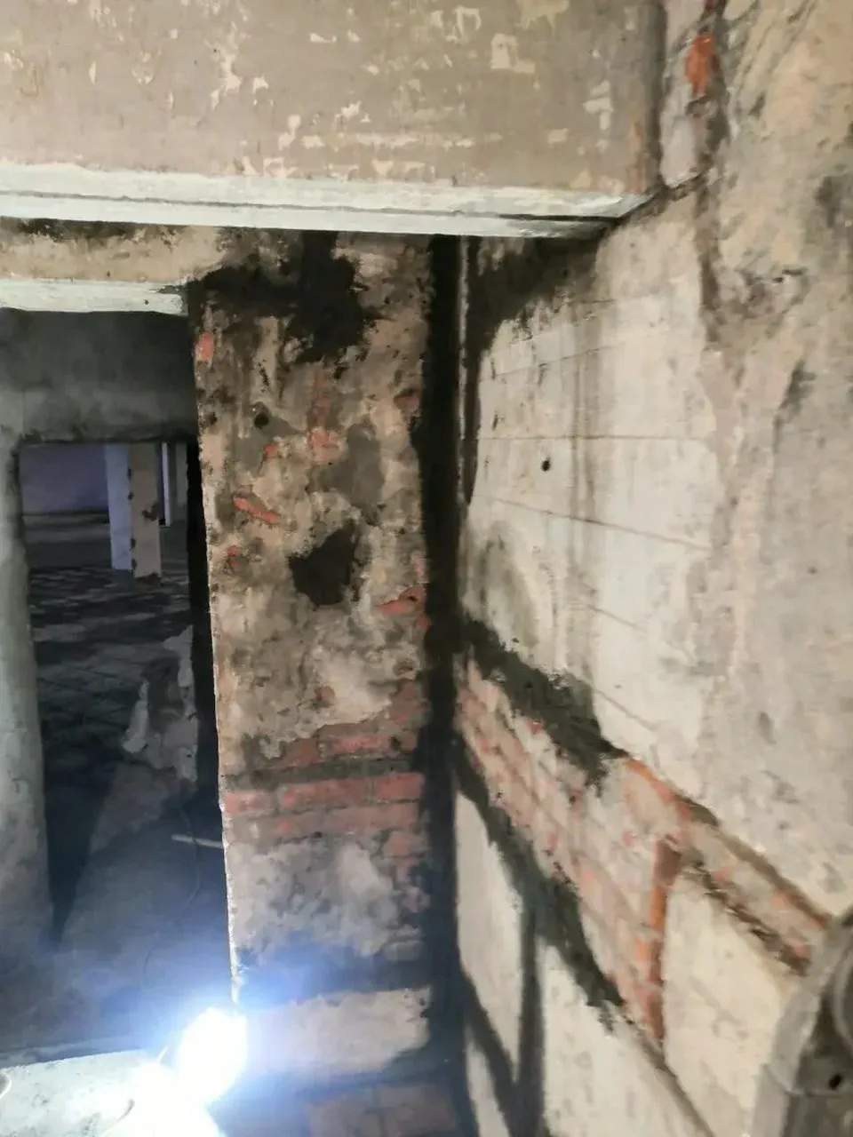 Повреждённая стена со следами увлажнения и открытой кладкой у проёма