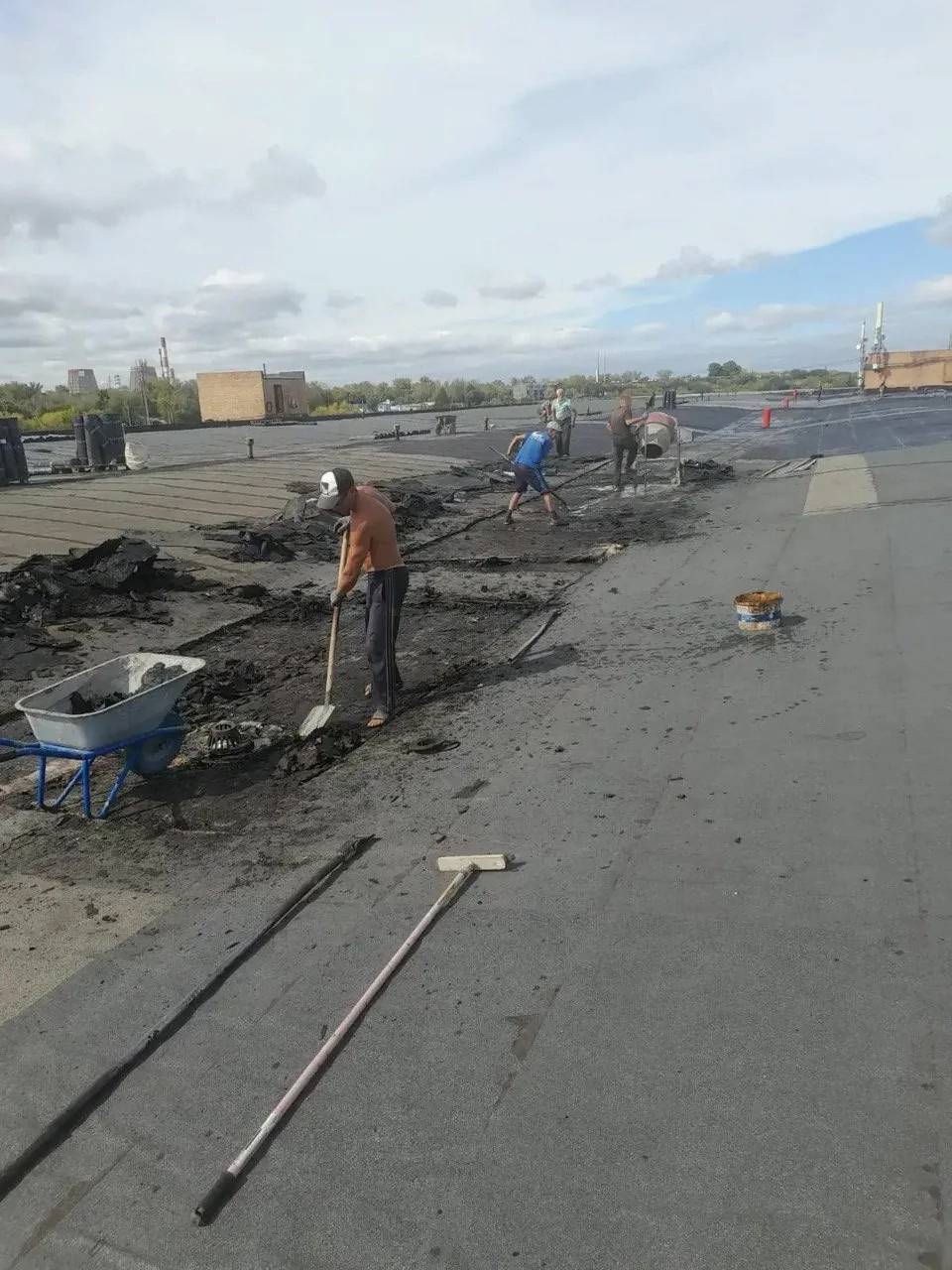 Рабочие разбирают повреждённые участки покрытия большой плоской кровли
